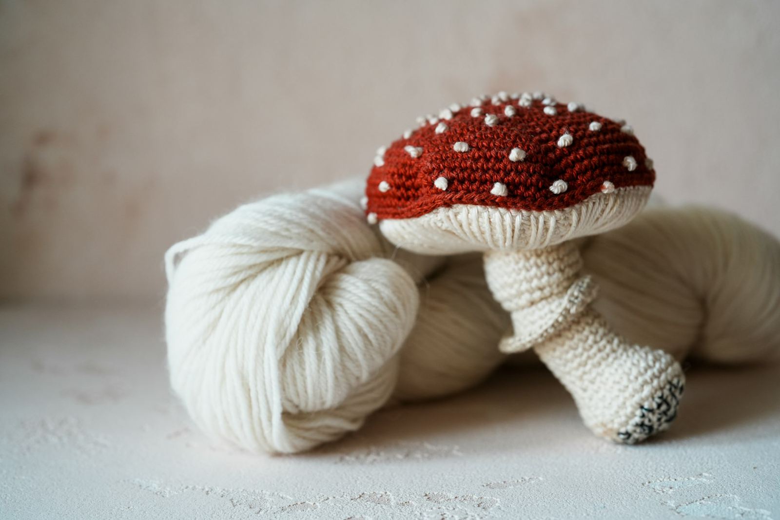A crocheted red mushroom resting on a skein of cream cotton yarn