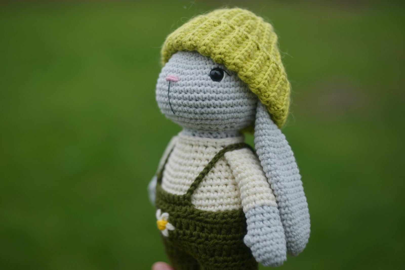 Crocheted grey bunny in a green knitted hat and olive overalls