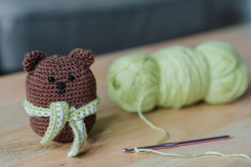 Small crochet bear next to a skein of mint yarn and a hook
