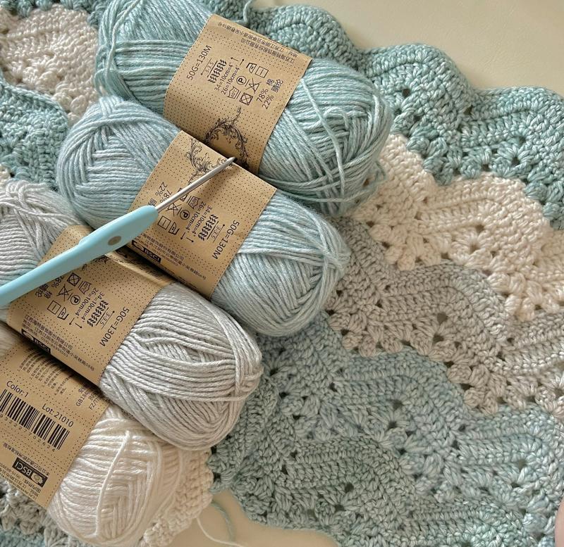 Skeins of pale blue cotton yarn with a crochet hook on a blanket