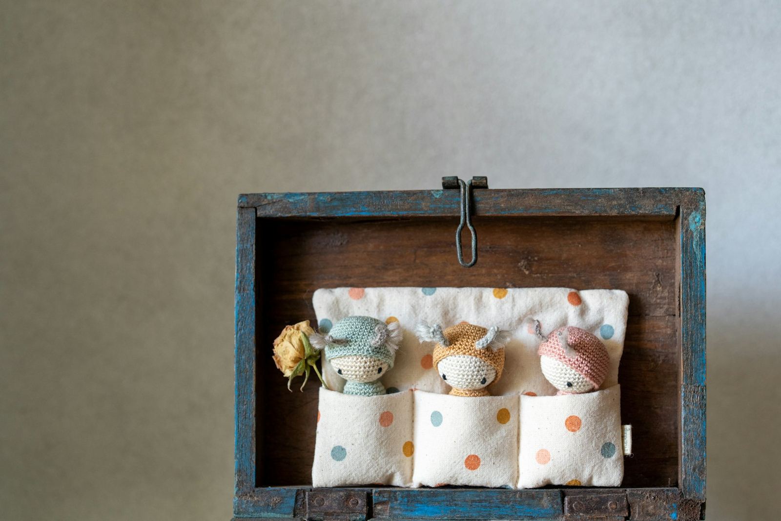 Three small crochet dolls tucked into a fabric sleeping bag inside a wooden box
